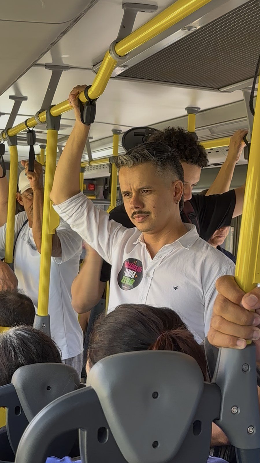 Fabrício viaja em pé dentro de um ônibus, segurando uma alça de apoio.