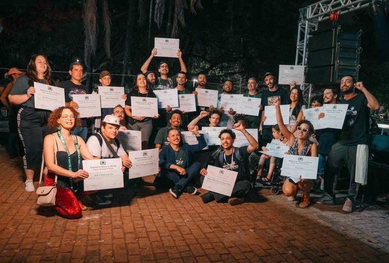 Participantes da homenagem antiproibicionista posam com diplomas em frente a um palco.
